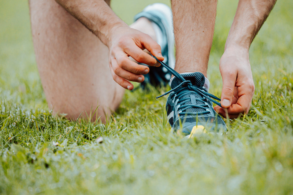 person kneels on grass to tie their shoelaces