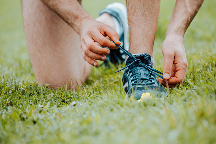 person-kneels-on-grass-to-tie-their-shoe