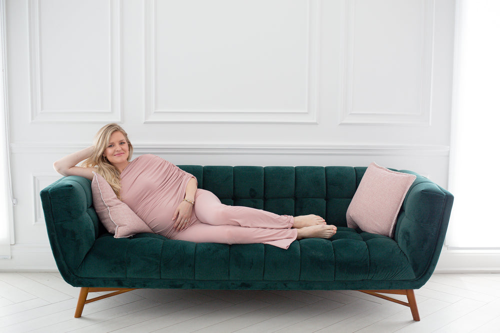 person lays on a dark green couch and smiles