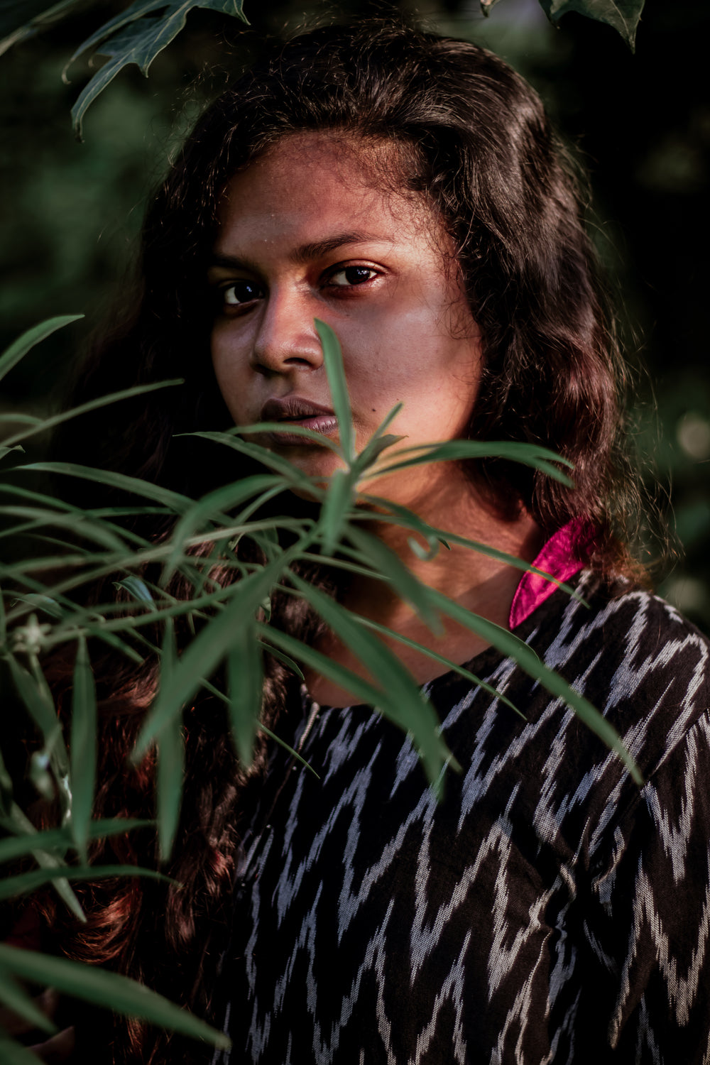 person looks at the camera through the leaves of a plant