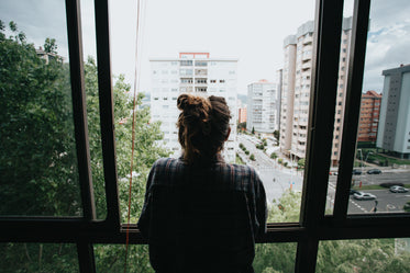 person looks out an open window toward city below