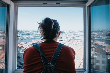 person looks out open window to the city below