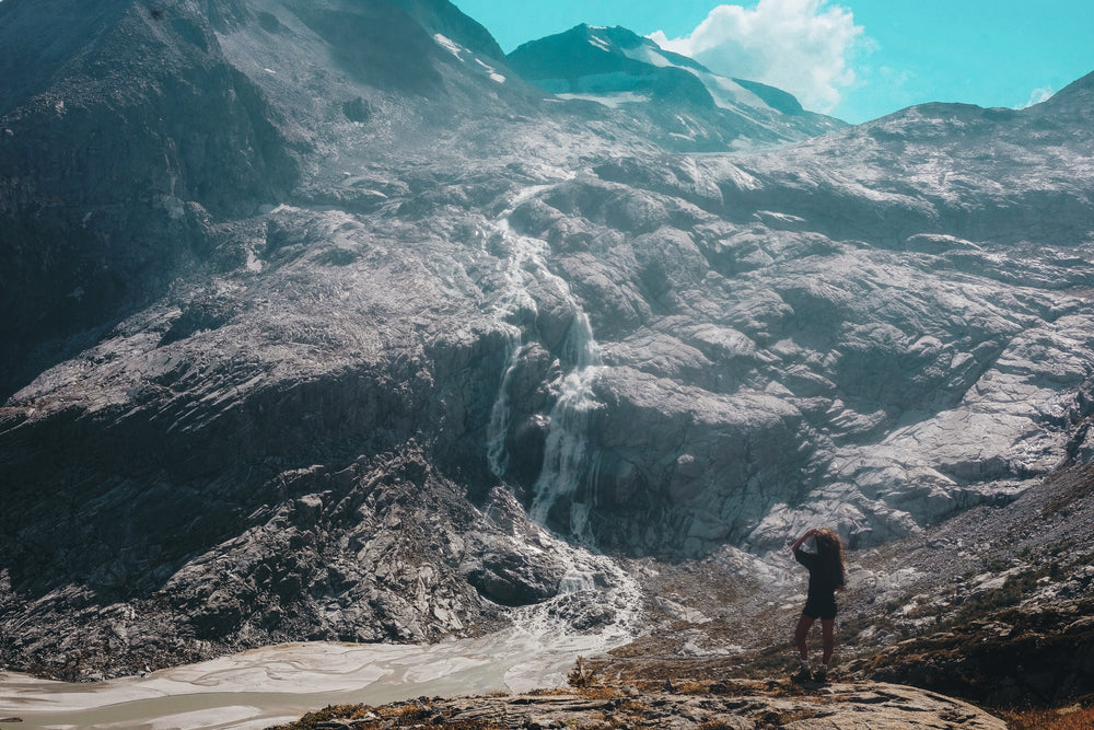 person looks up to see a mountain side waterfall