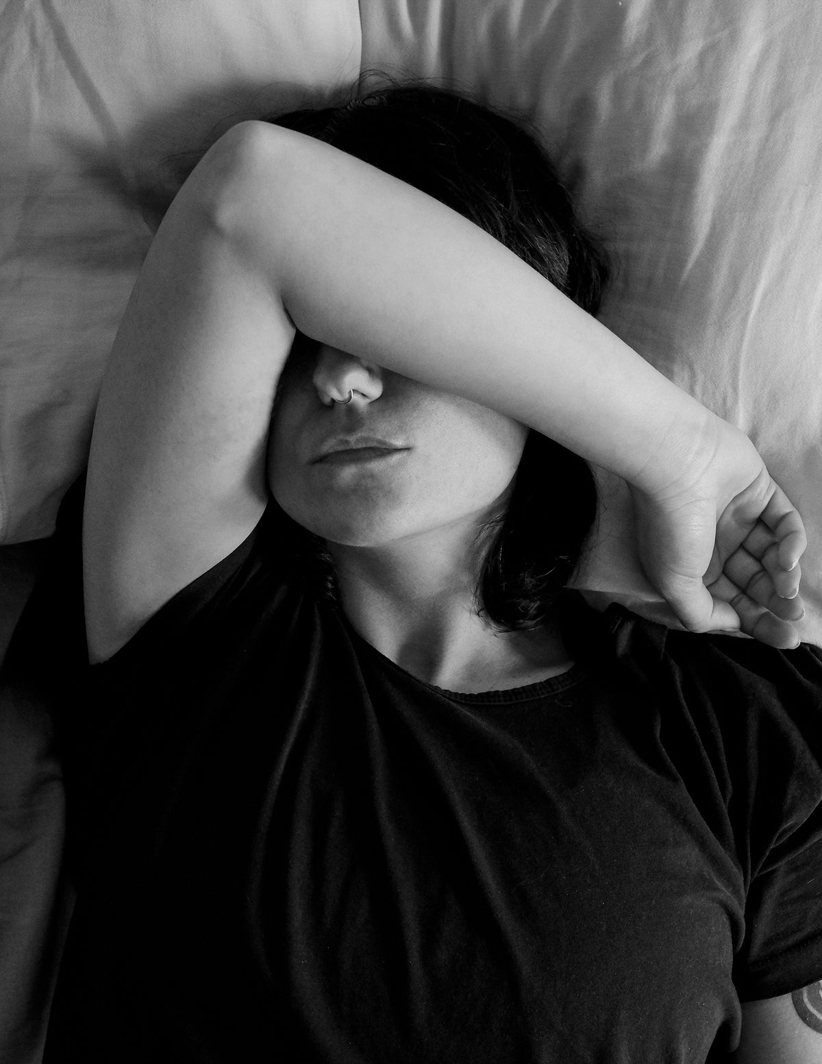 person lying with their arm up in bed in black and white