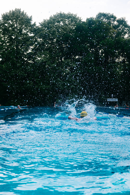 person makes large splashes while swimming lengths outdoors