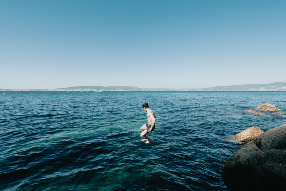 person mid air jumping into clear blue water