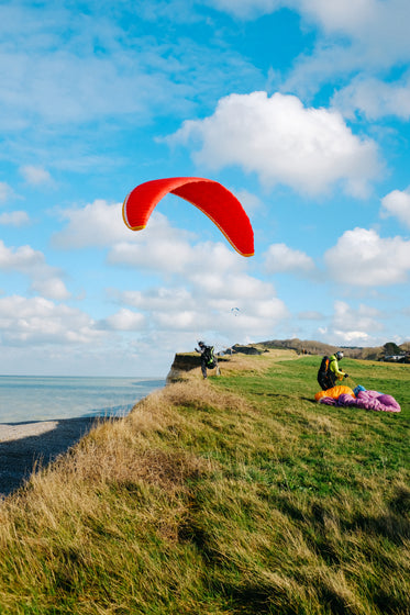 person on a grassy hill with a red kite