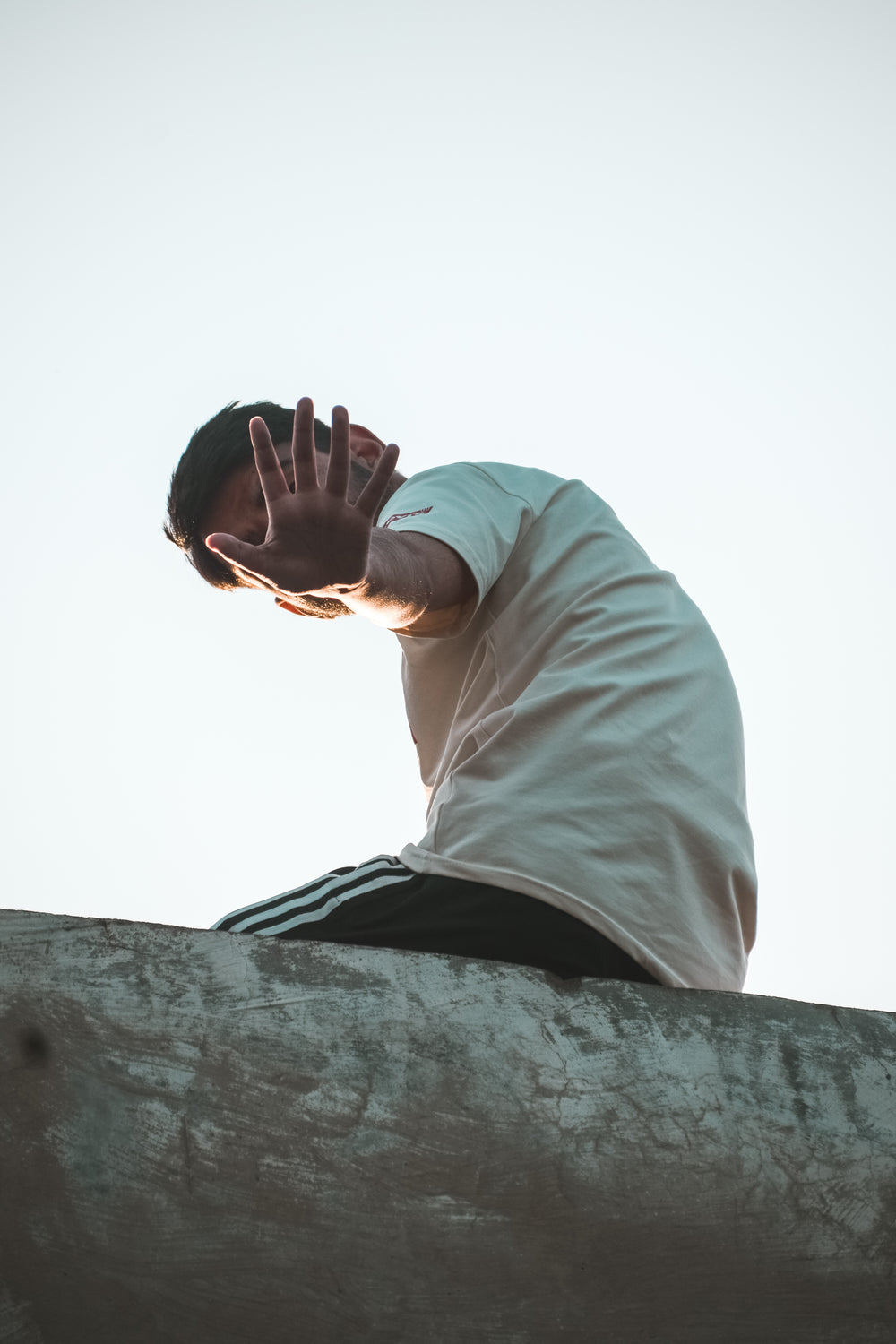 person on a ledge hand up to hide their face