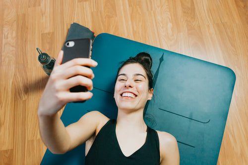 person on a yoga mat smiles at their cell phone
