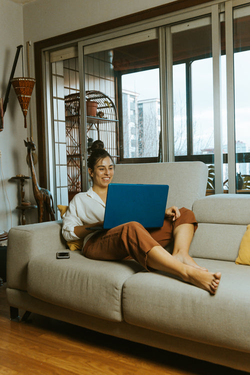 person on couch smiles at laptop screen