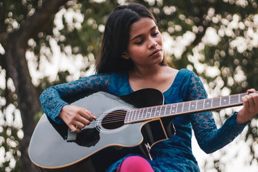 person plays the guitar outdoors under trees