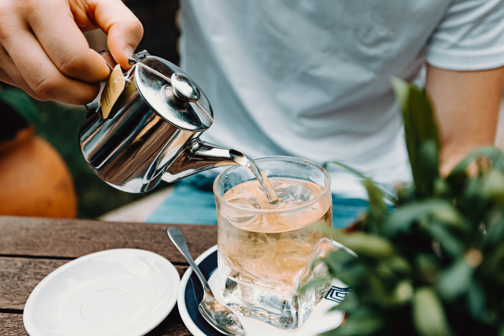 person pours tea into glass outdoors