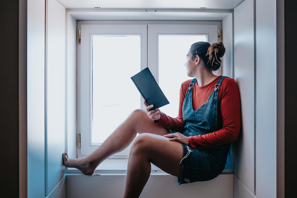 person reads a book sitting in a window alcove