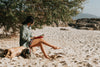 person reads their novel sitting on a sandy beach