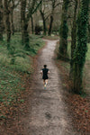 person runs if a lush green forest with a dirt pathway