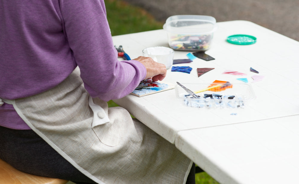 person sits at a white workbench and works on a mosaic