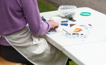 person sits at a white workbench and works on a mosaic