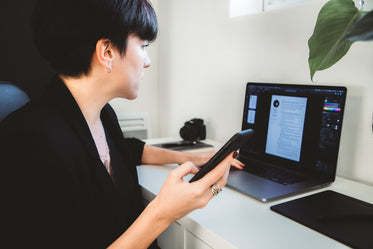 person sits at desk with a laptop and holds their phone