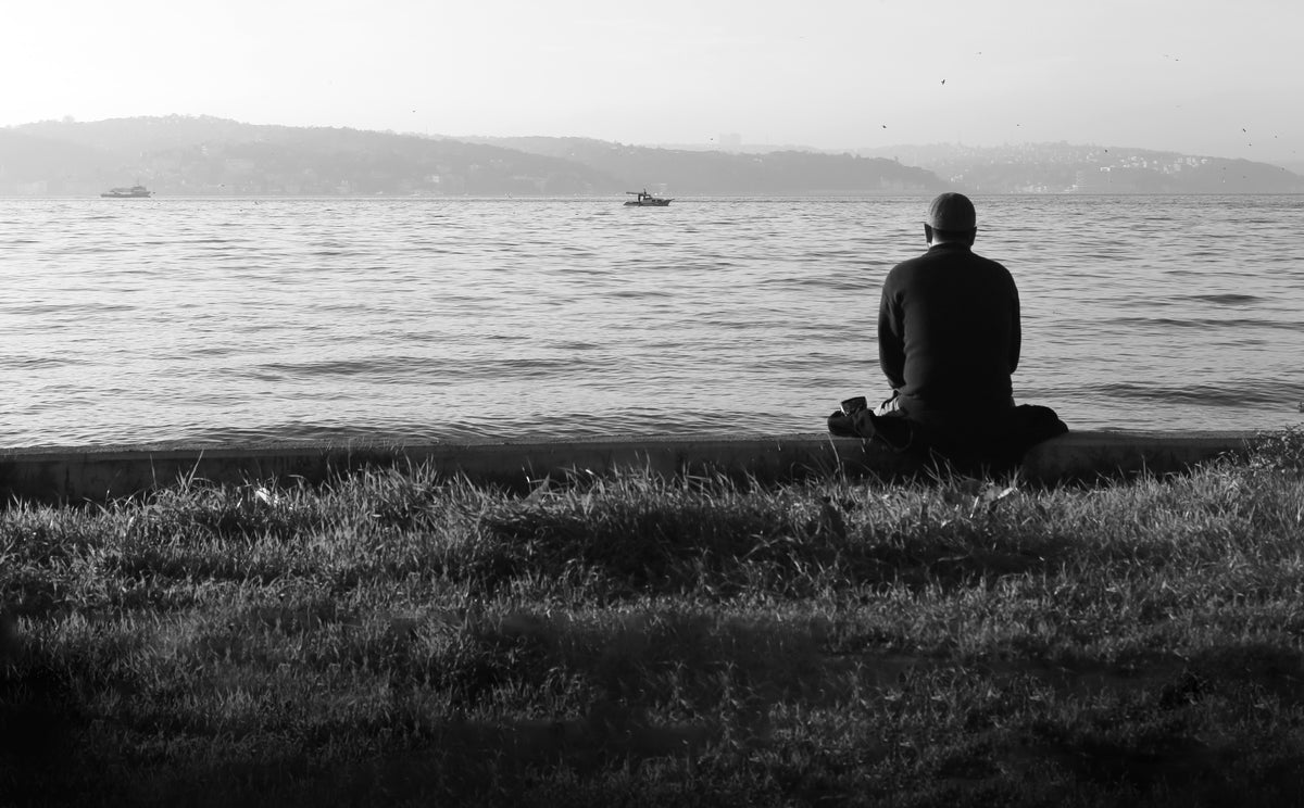 人坐着，望着平静的水面