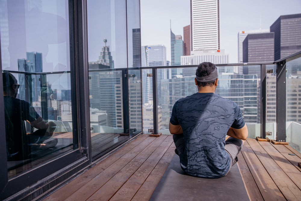 person sits on a grey yoga mat on a wooden deck