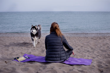 person sits on a mat at the beach and looks out to the water