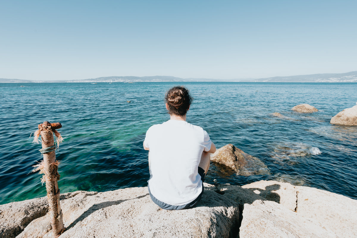 person sits on a rock and looks out to the water