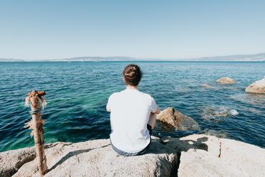 person sits on a rock and looks out to the water