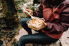 person sits on a rock outdoors and eats pasta salad