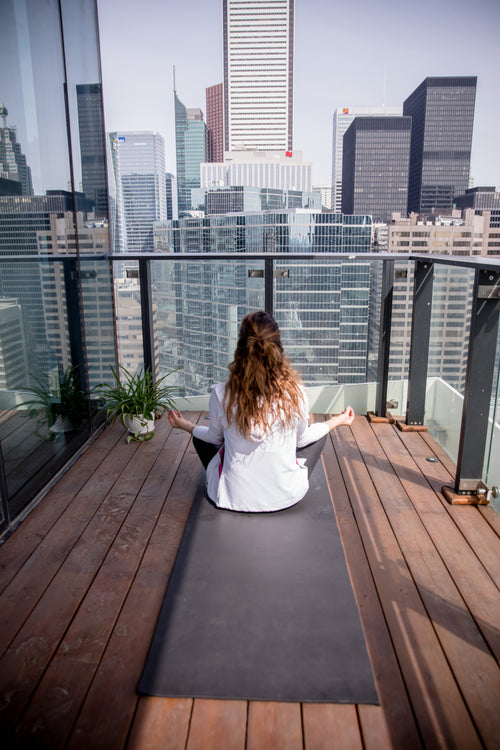 person sits on a yoga mat on there wood floored balcony