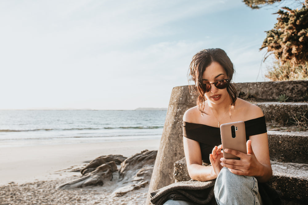 person sits on steps by a beach looking at their phone