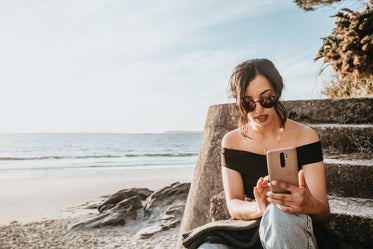 person sits on steps by a beach looking at their phone