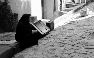 person sits on the sidewalk next to suitcases