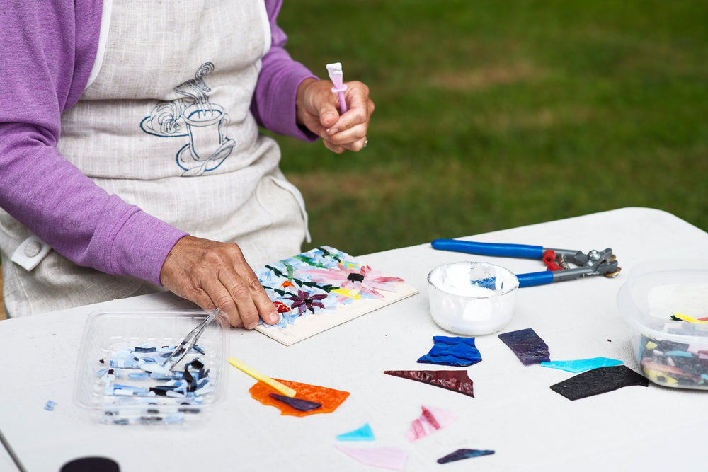 person sits outdoors and works on a floral glass mosaic