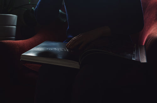 person sits with a large book in their lap in the dark