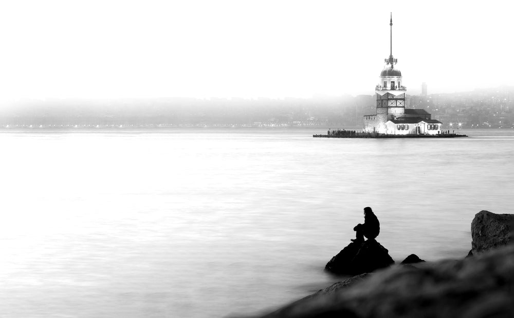 person sitting by still body of water in monochrome