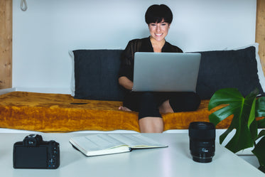person sitting on a gold couch smiles working on their laptop
