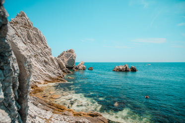 person snorkels off white rocky shoreline