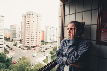 person standing by a window with their hand to their head