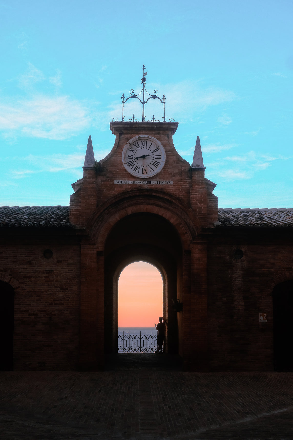 person standing in a courtyard archway at sunset
