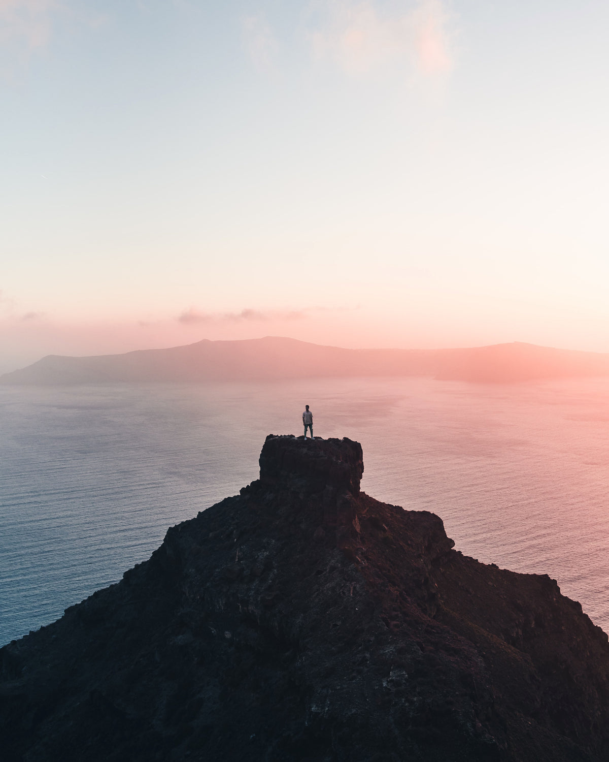person standing on a far cliff taking a the setting sun