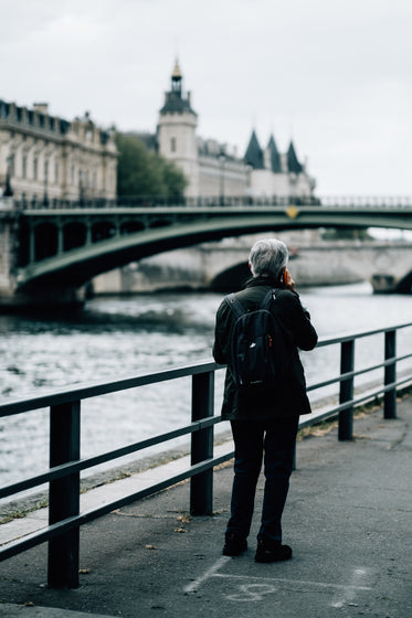 person stands by a river while chatting on their phone