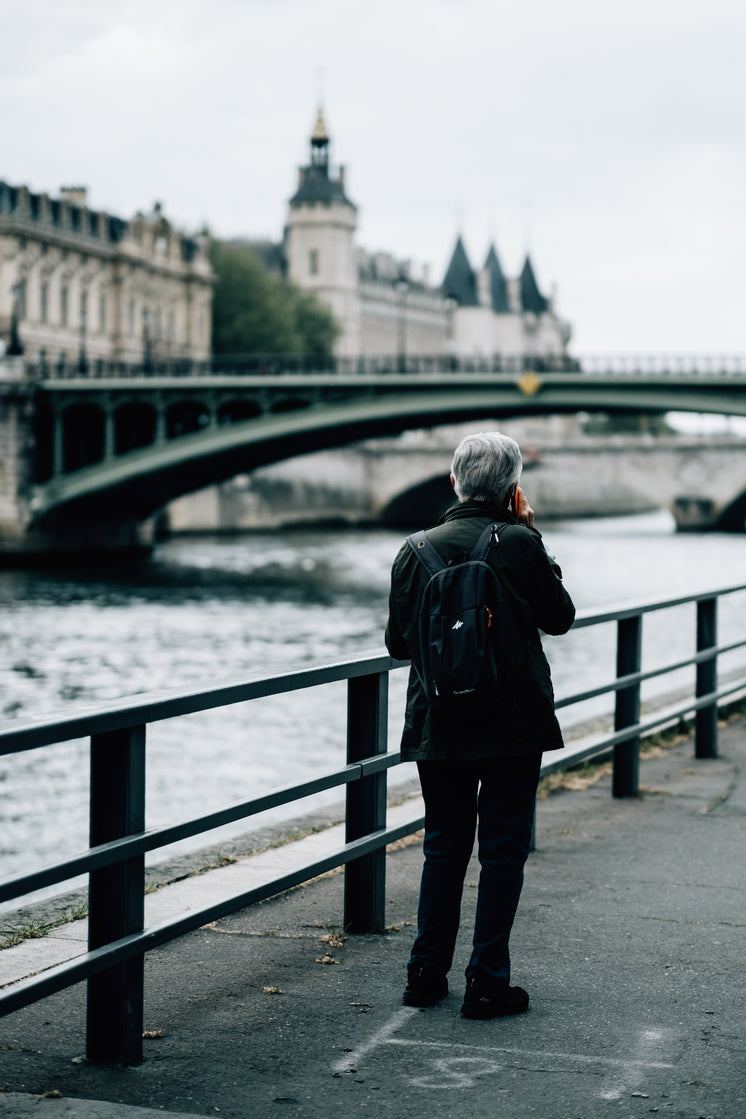 Person Stands By A River While Chatting On Their Phone