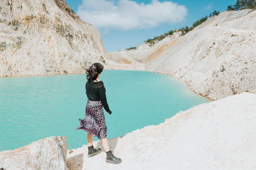 person stands by a still lake of blue water