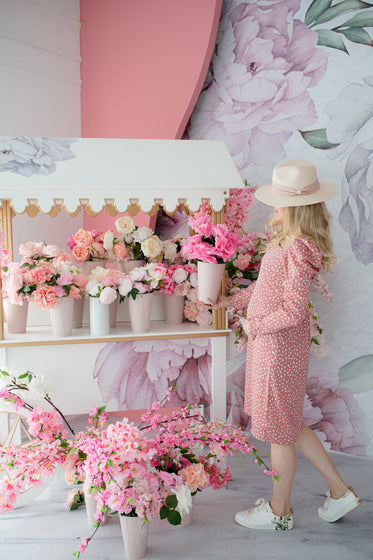 person stands by pink flower stand in polka dot dress