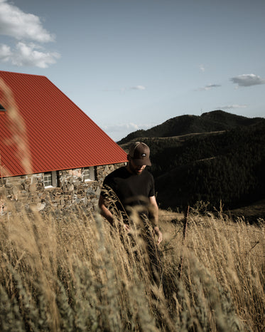 person stands in golden wheat with a building behind