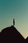 person stands on a hill top silhouetted below aqua sky
