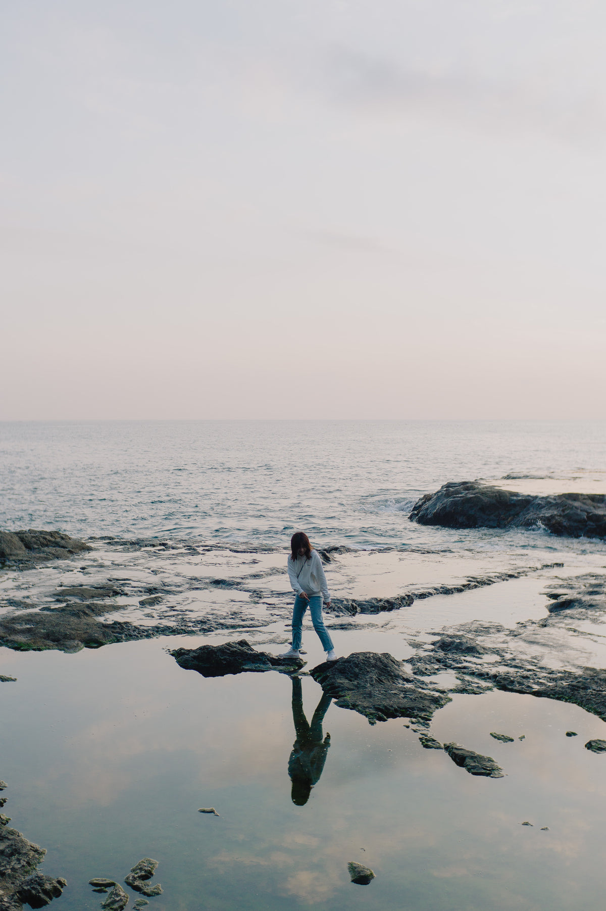 person stands on rocks poking out of the ocean shoreline