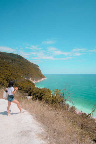 person stands on white sandy hill looking out to the ocean