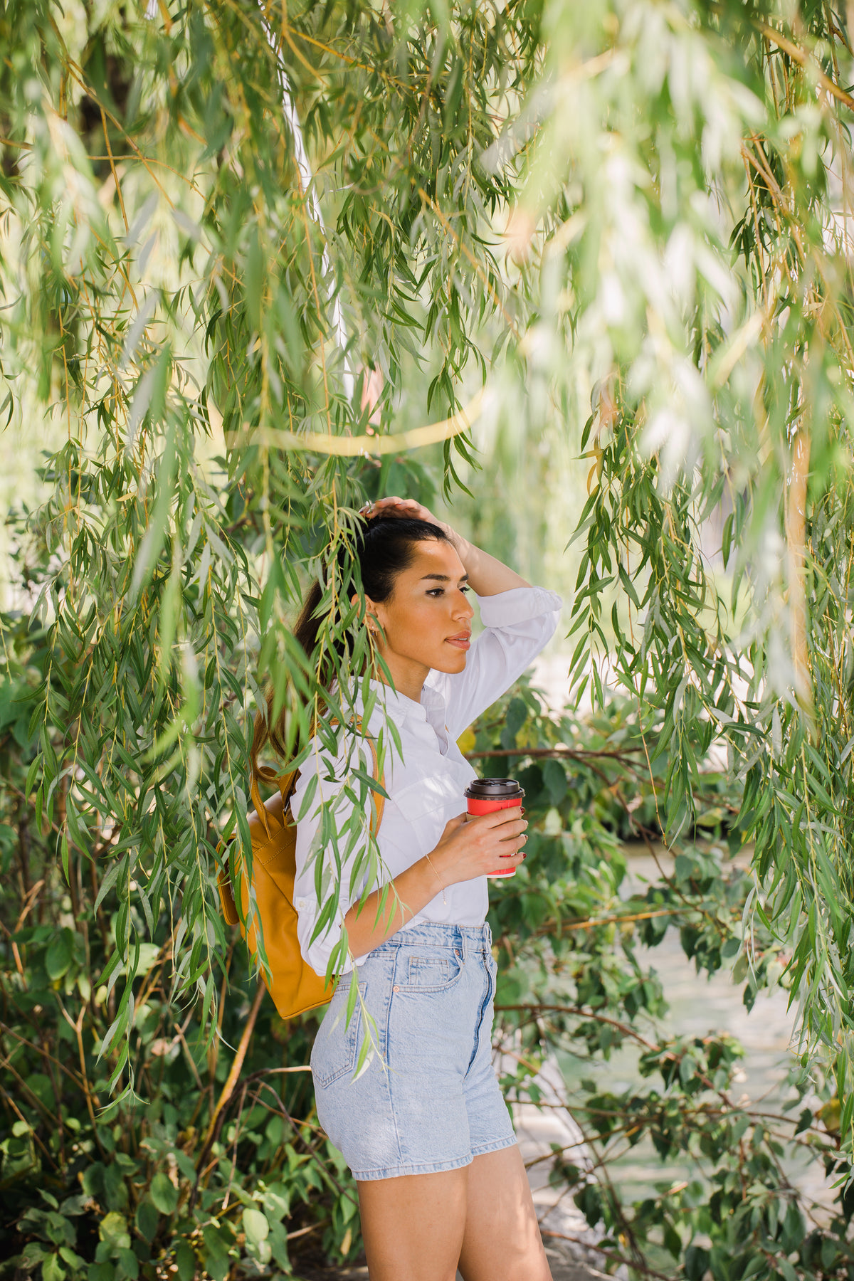 person stands surrounded by willow tree leaves