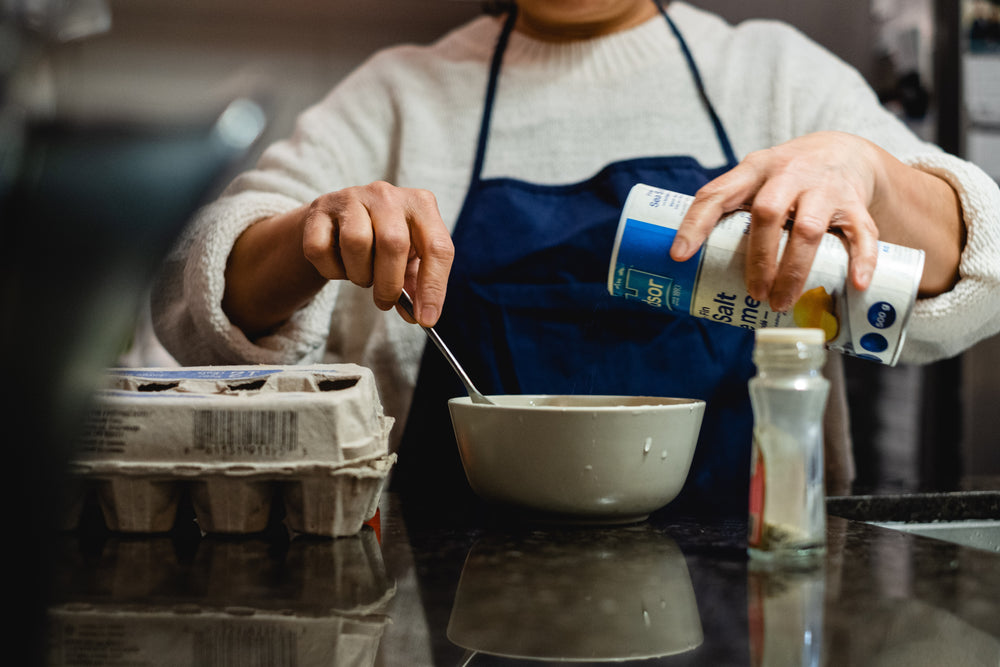 person stirs a bowl and holds salt to pour